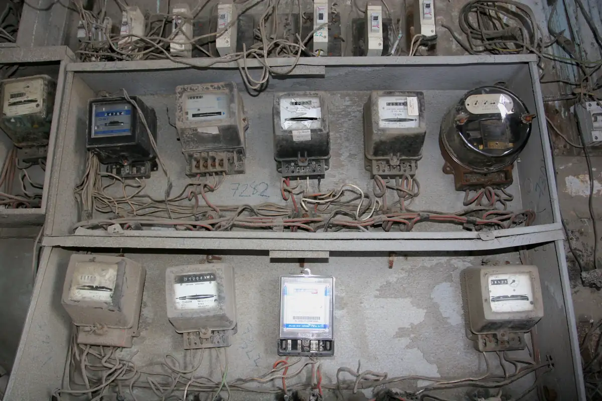 A dusty wall cabinet in Havana holding two rows of old electricity meters of different makes, joined by tangled wiring.