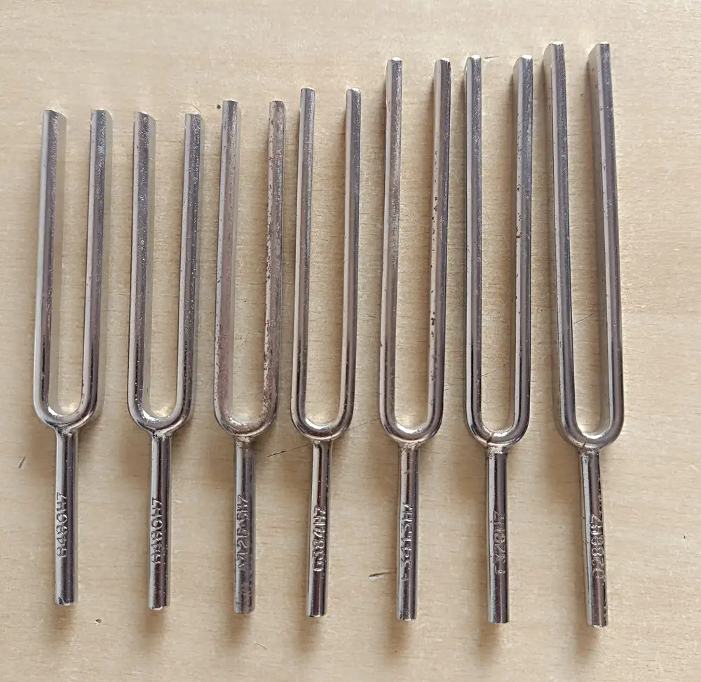 Seven steel tuning forks of increasing length laid side by side on a pale wooden surface.