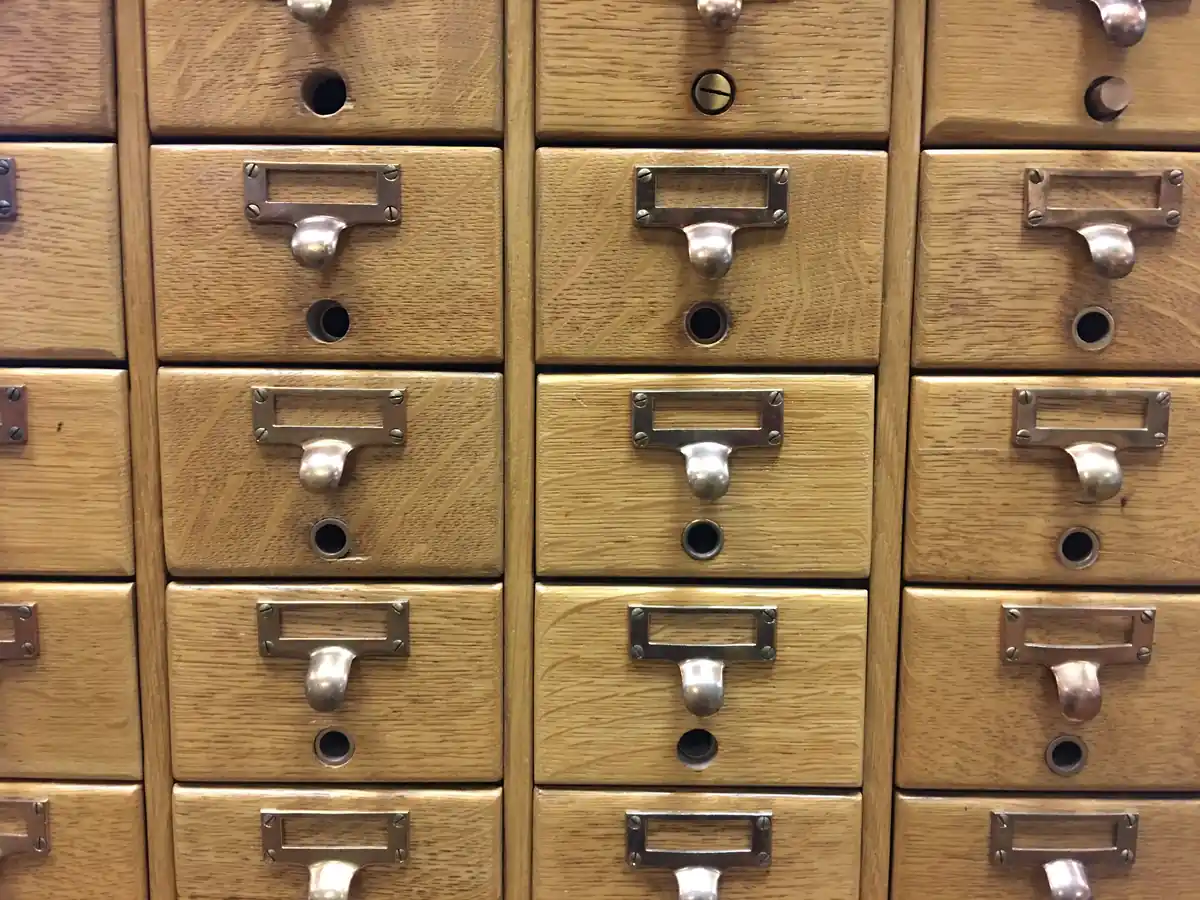 Rows of wooden library card catalog drawers, each with a brass label holder and pull handle.