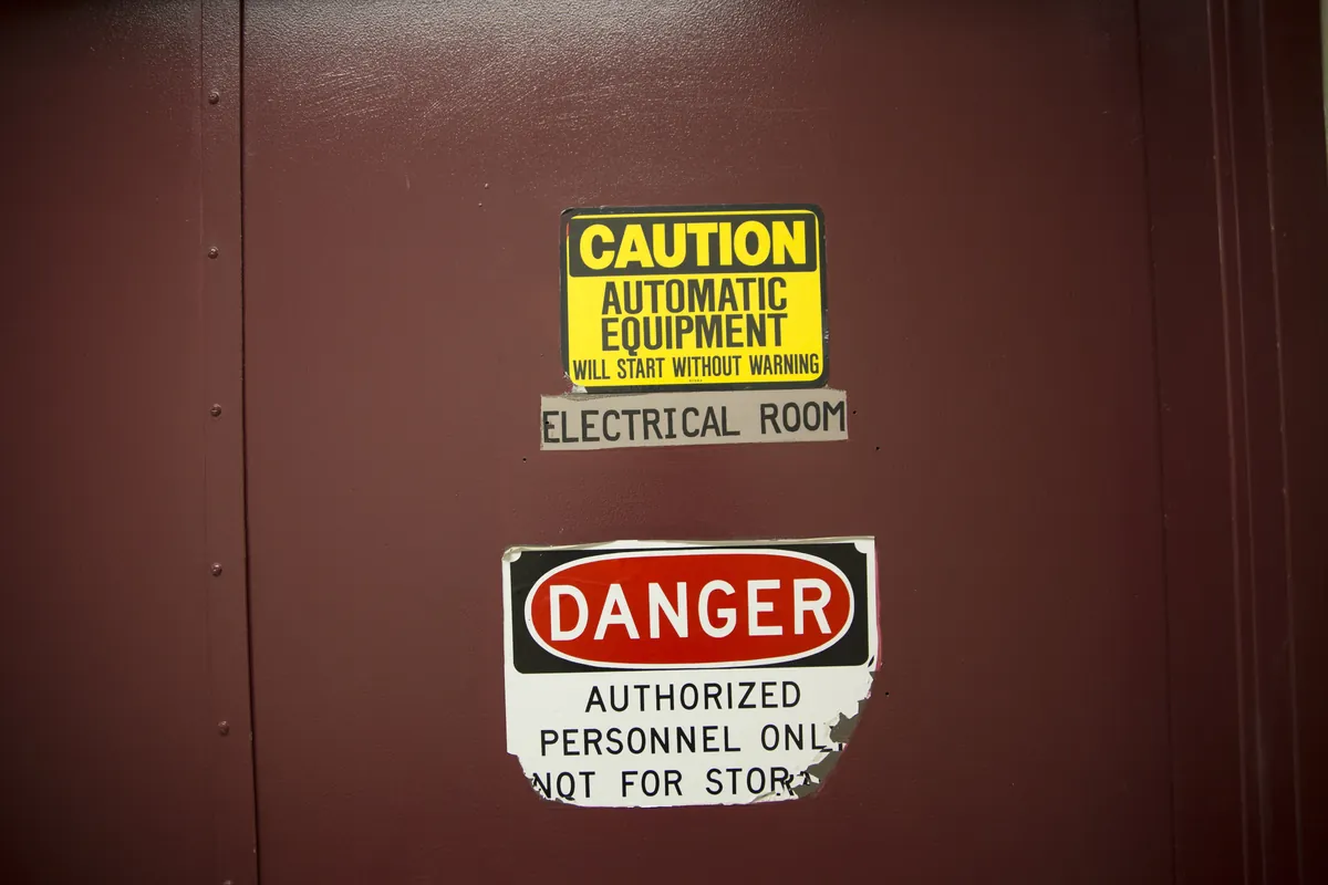 Signs on a dark red door reading Caution: automatic equipment will start without warning, Electrical room, and Danger: authorized personnel only.
