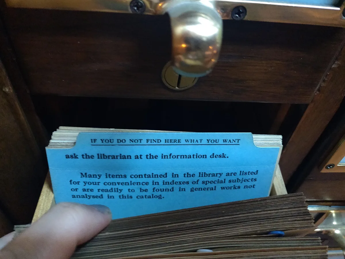 A blue guide card in an open card catalogue drawer reading: if you do not find here what you want, ask the librarian at the information desk.