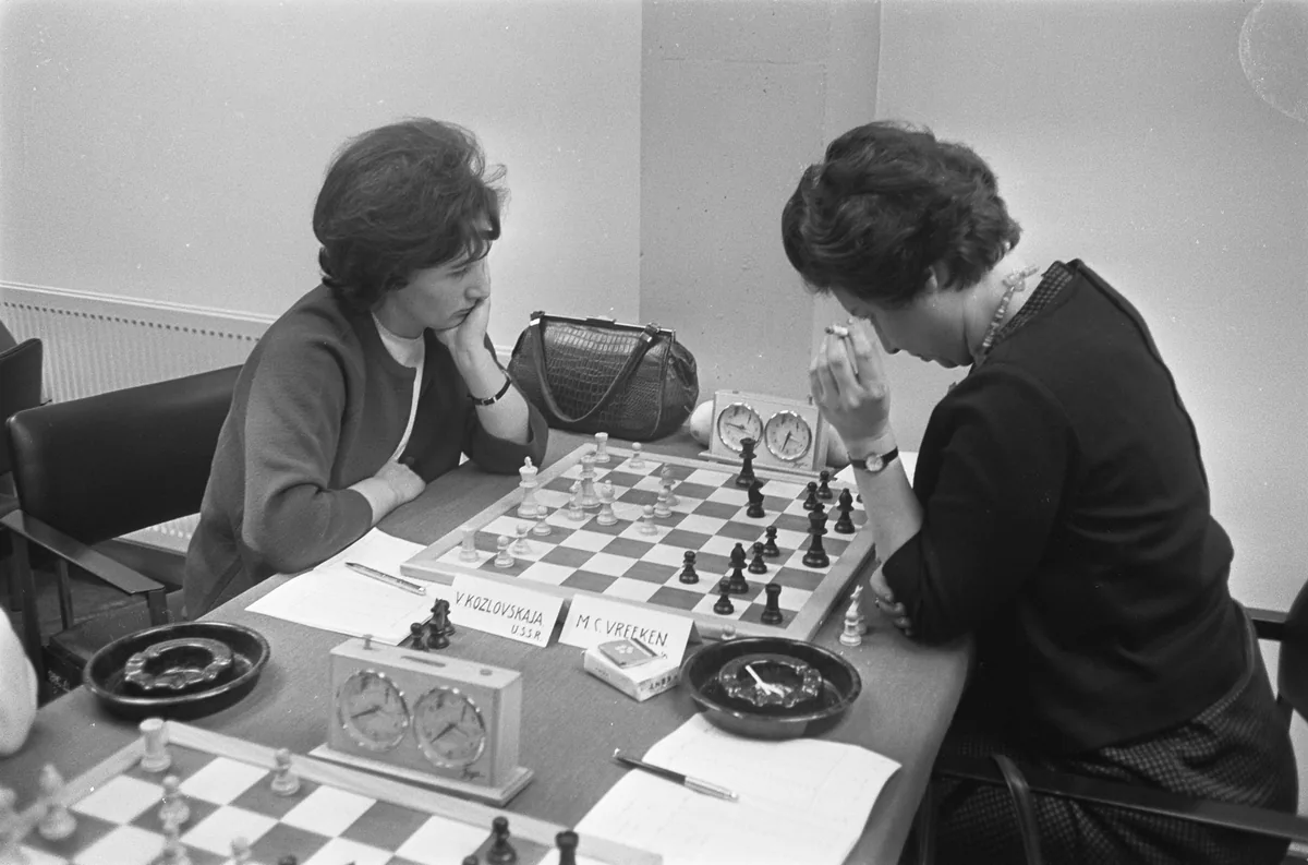 Two chess players deep in thought over a board, with clocks and handwritten score sheets on the table.