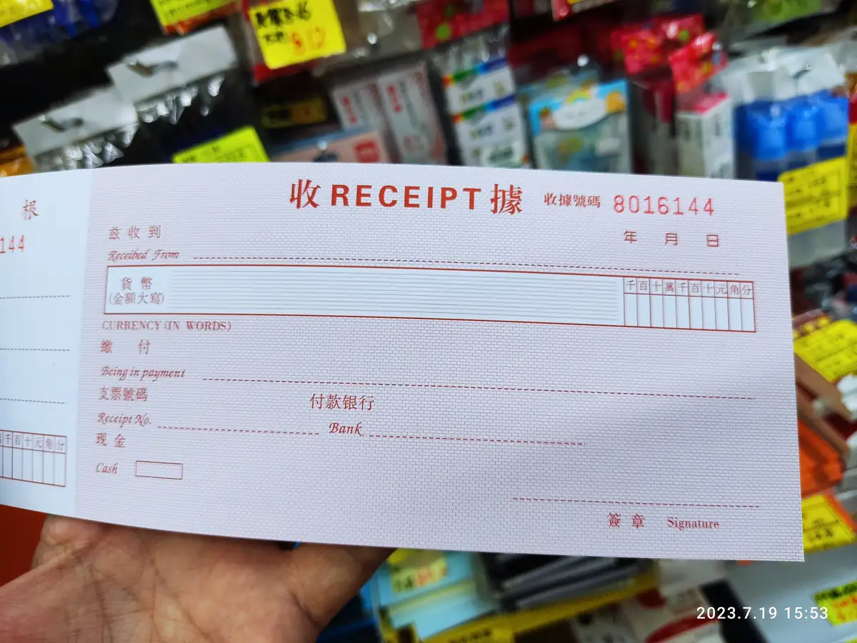 A blank bilingual receipt book held up in front of a stationery shop's shelves.