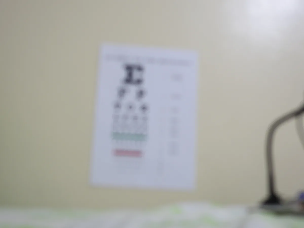 An eye chart on a clinic wall, photographed so far out of focus that only the large letter at the top is recognisable.
